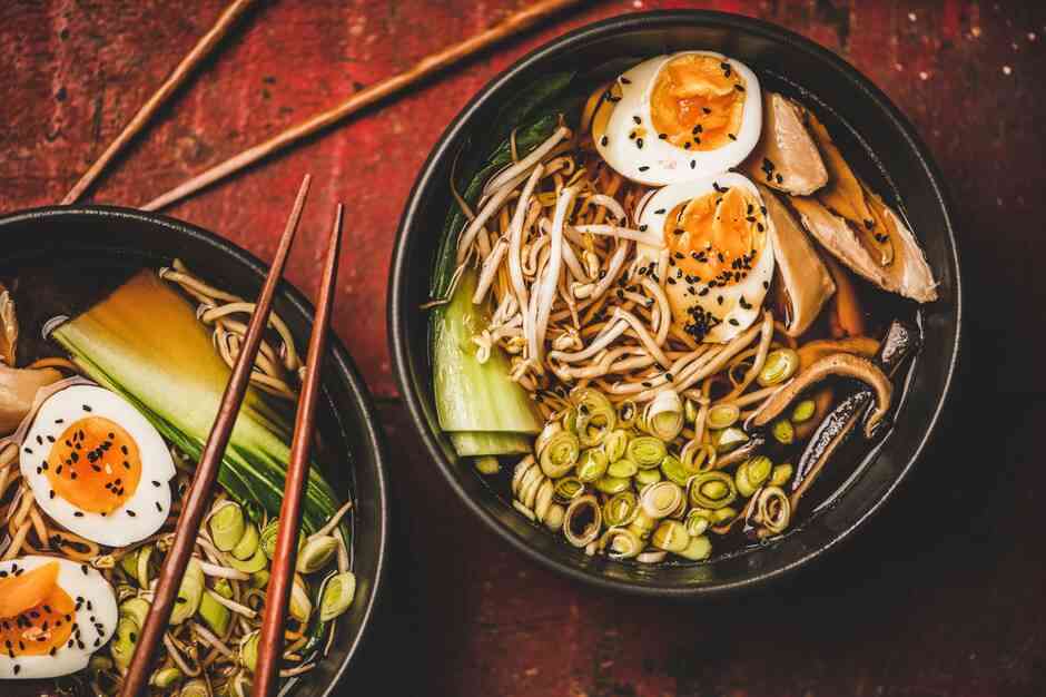 Ramen z mięsem z kurczaka jaja grzyby shiitake w czrnych miskach i bambusowe pałeczki na stole